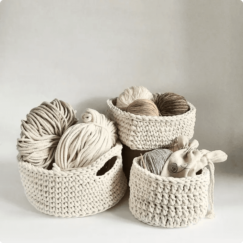 Na zdjęciu trzy jasne koszyczki z włóczki, a w nich motki włóczek w kolorach bieli, beżu, brązu i szarości.