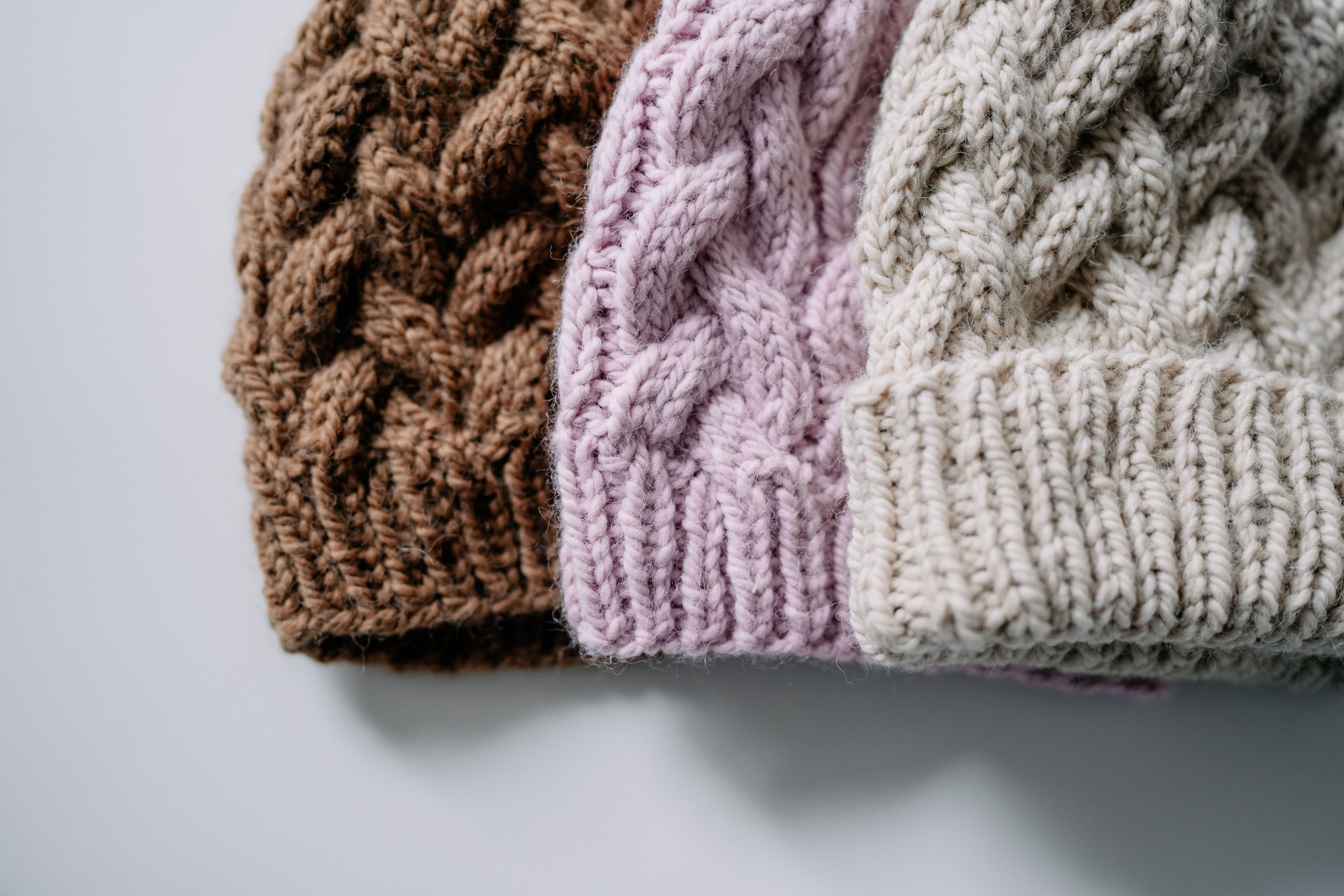 Na zdjęciu trzy grube, zimowe czapki w kolorze brązu, różu i beżu.